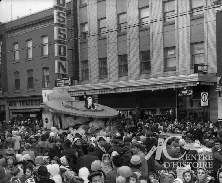 En foule pour voir le Père Noël.1960. - Fonds Raymond Bélanger, CH548.Lors du défilé du Père Noël, en 1960, plus de 20 000 personnes assistent aux festivités entourant l'événement. Ici, le Père-Noël salue la foule à l'angle des rues St-François et des Cascades.
