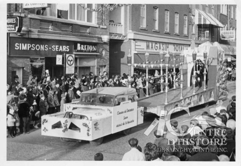 Un premier défilé en 1955.1966. - Fonds Le Courrier de Saint-Hyacinthe, CH380.Bien que cette photo témoigne du défilé de 1966, c'est en 1955 que se déroule le premier défilé du Père-Noël à Saint-Hyacinthe. L'événement populaire commence au Manège militaire où le Père-Noël arrive en hélicoptère!
