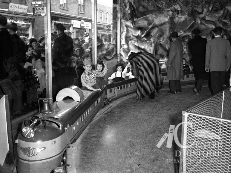Un train miniature au Palais du Père Noël. 1956. - Fonds Raymond Bélanger CH548.En 1956, les enfants qui visitent le Palais du Père Noël peuvent faire une petite balade dans le train électrique. Ce train n'est pas sans rappeler le « petit train à Gervais » qui déservait le parc Laframboise vers 1912.